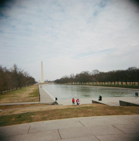 Image of people setting by a body of water next to the Washington Monument 